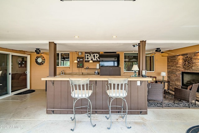 kitchen featuring a kitchen bar, ceiling fan, wooden walls, and an outdoor stone fireplace