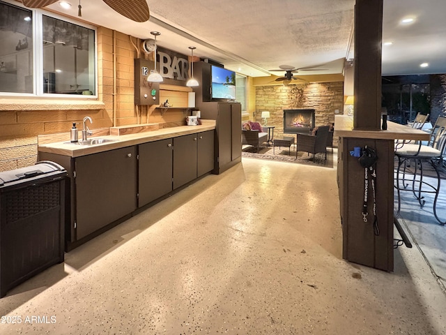 kitchen featuring ceiling fan, a textured ceiling, a stone fireplace, a sink, and hanging light fixtures