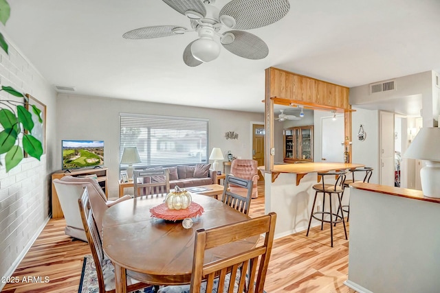 dining space with brick wall, light wood finished floors, visible vents, and a ceiling fan