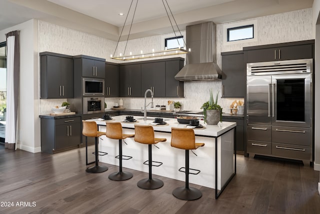 kitchen with wall chimney range hood, a breakfast bar, dark wood-style floors, and stainless steel appliances