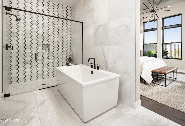 ensuite bathroom featuring a tile shower, tile walls, a soaking tub, a chandelier, and ensuite bath