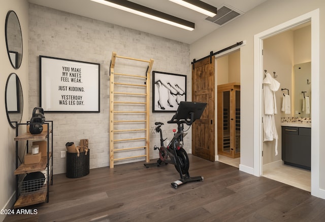 exercise area featuring visible vents, a barn door, wood finished floors, brick wall, and baseboards