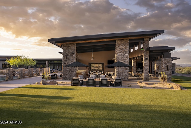 back of property at dusk featuring a patio, a yard, and stone siding