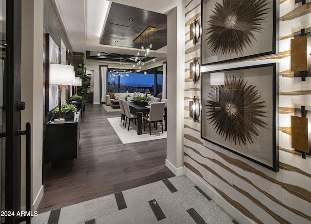 corridor featuring a tray ceiling, baseboards, and a notable chandelier