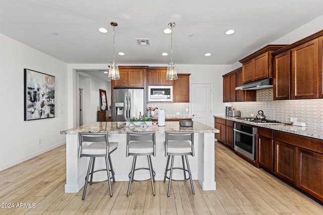 kitchen featuring appliances with stainless steel finishes, hanging light fixtures, tasteful backsplash, and light hardwood / wood-style flooring