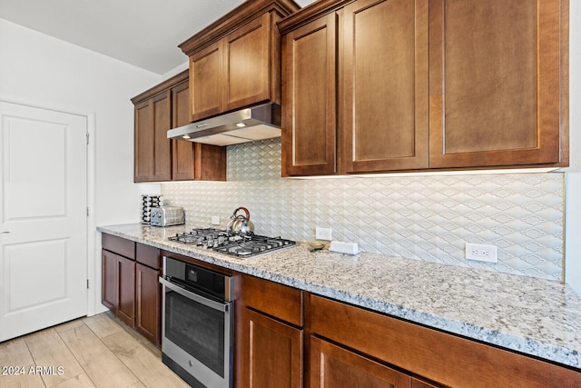 kitchen featuring appliances with stainless steel finishes, light stone countertops, tasteful backsplash, and light wood-type flooring