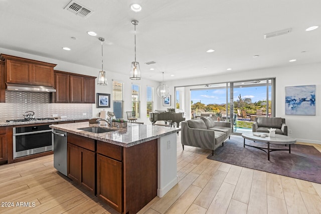 kitchen featuring light stone counters, stainless steel appliances, backsplash, a kitchen island with sink, and sink