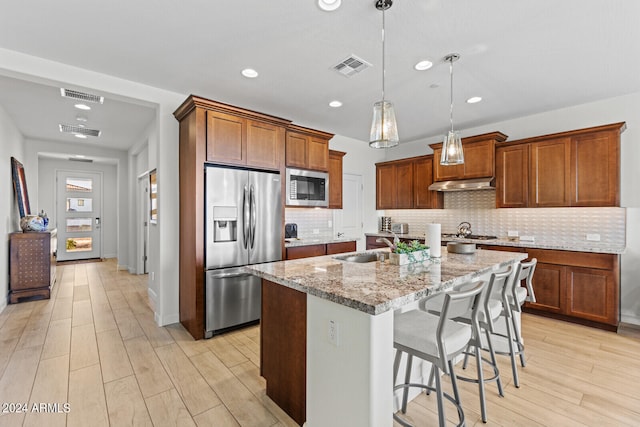 kitchen featuring an island with sink, stainless steel appliances, pendant lighting, backsplash, and a breakfast bar area