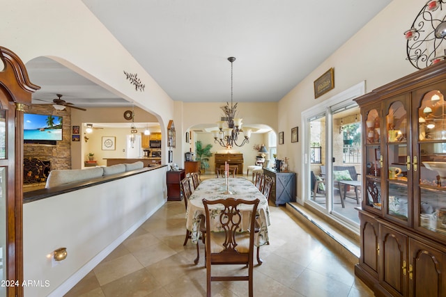 tiled dining space with ceiling fan with notable chandelier and a fireplace