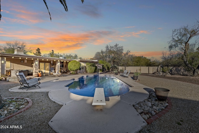 pool at dusk with a diving board and a patio