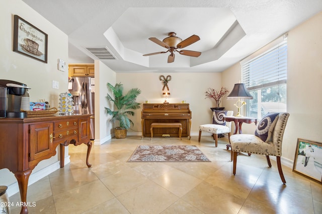 living area with light tile flooring, ceiling fan, and a tray ceiling