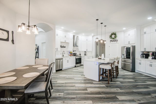 kitchen featuring wall chimney exhaust hood, appliances with stainless steel finishes, a breakfast bar, a center island, and a sink