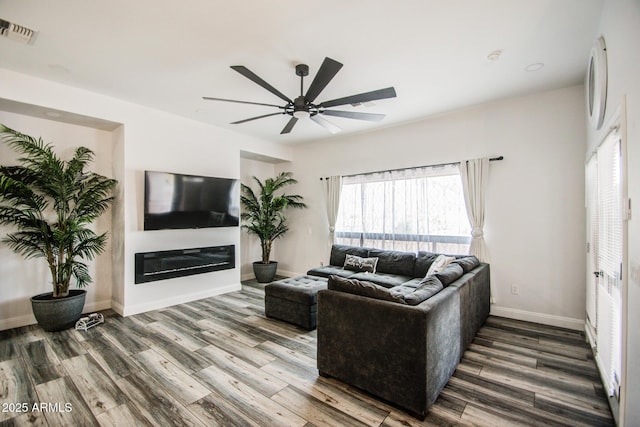 living area featuring a ceiling fan, visible vents, wood finished floors, and a glass covered fireplace