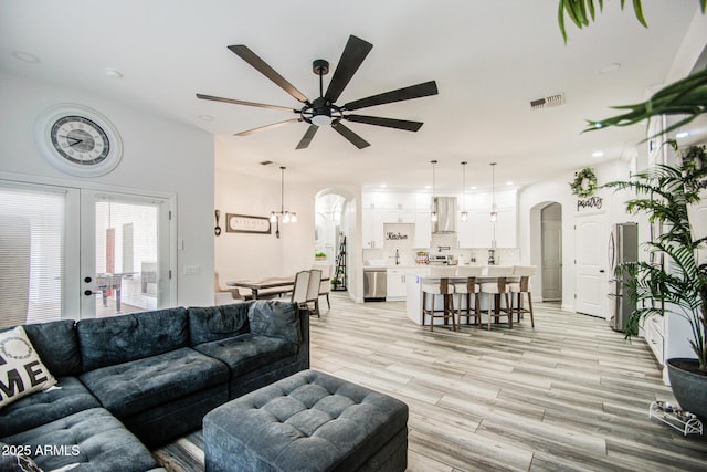 living room featuring light wood-type flooring, visible vents, arched walkways, and ceiling fan