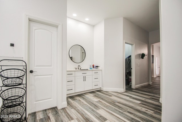 bathroom with a walk in closet, recessed lighting, vanity, wood finished floors, and baseboards