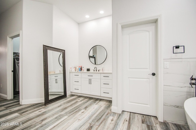 full bath featuring wood finished floors, a walk in closet, vanity, a freestanding tub, and recessed lighting