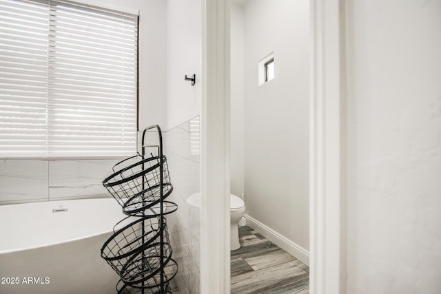 bathroom featuring toilet, baseboards, a freestanding bath, and wood finished floors