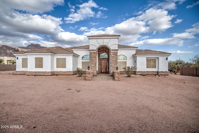 mediterranean / spanish-style house with stone siding, a tiled roof, and stucco siding