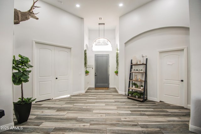 foyer featuring arched walkways, recessed lighting, a towering ceiling, wood finished floors, and baseboards