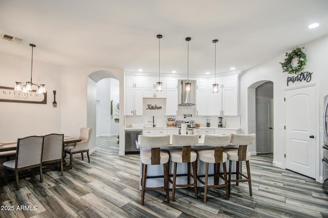 kitchen featuring tasteful backsplash, visible vents, arched walkways, stainless steel appliances, and wall chimney range hood