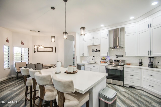 kitchen featuring wall chimney exhaust hood, tasteful backsplash, light countertops, appliances with stainless steel finishes, and a kitchen breakfast bar