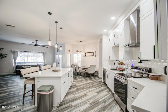 kitchen with light countertops, visible vents, decorative backsplash, wall chimney range hood, and stainless steel range with electric stovetop