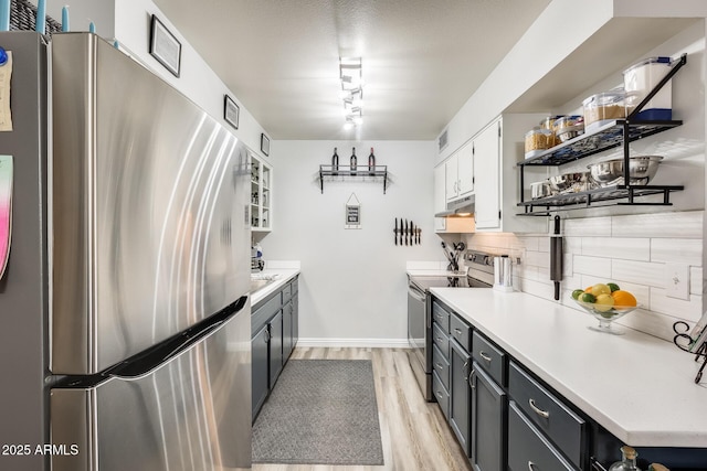 10374 W Deanne Dr, Sun City, AZ 85351 - kitchen featuring light wood finished floors, stainless steel appliances, under cabinet range hood, open shelves, and backsplash