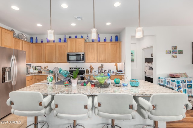 kitchen featuring light brown cabinets, a center island with sink, a kitchen breakfast bar, pendant lighting, and stainless steel appliances