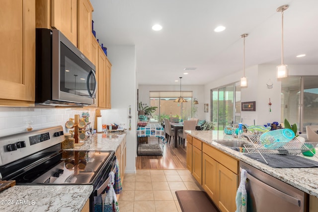 kitchen with hanging light fixtures, stainless steel appliances, backsplash, light wood-type flooring, and light stone counters