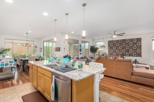 kitchen featuring light wood-type flooring, a wealth of natural light, stainless steel dishwasher, and a kitchen island with sink