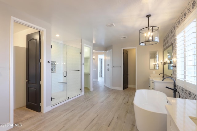 bathroom with shower with separate bathtub, vanity, wood-type flooring, and an inviting chandelier