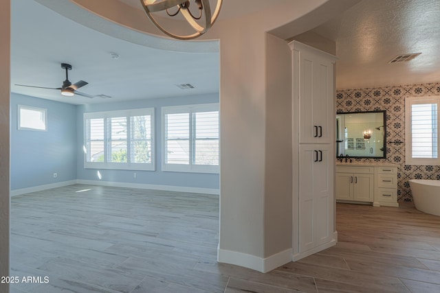 corridor featuring sink, light wood-type flooring, a chandelier, and a textured ceiling