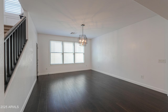 spare room with an inviting chandelier and dark hardwood / wood-style floors