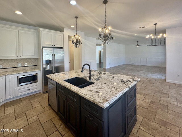 kitchen with stainless steel appliances, a center island with sink, white cabinetry, ceiling fan with notable chandelier, and sink