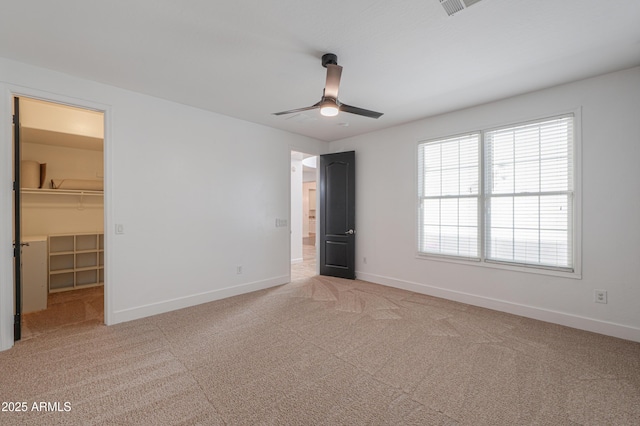 unfurnished bedroom with a walk in closet, a closet, ceiling fan, and light colored carpet