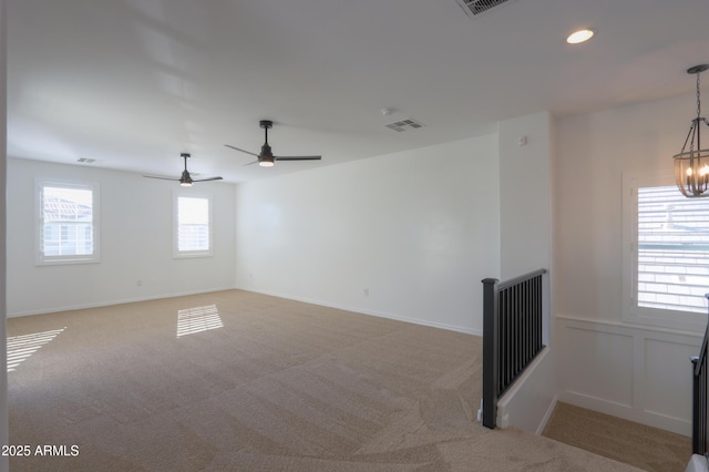 carpeted empty room featuring ceiling fan with notable chandelier