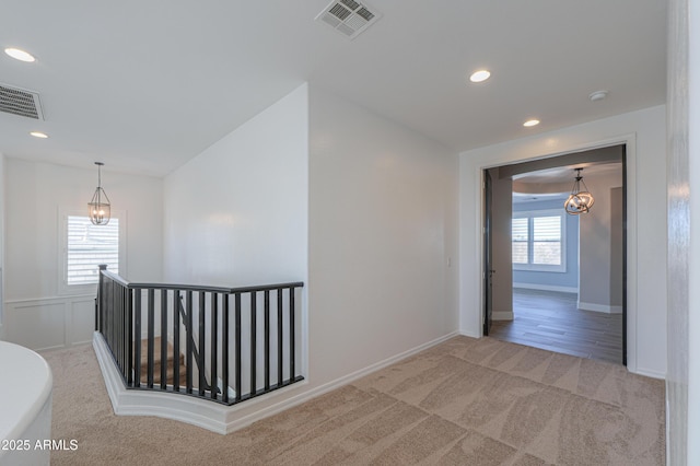 corridor featuring an inviting chandelier and light colored carpet