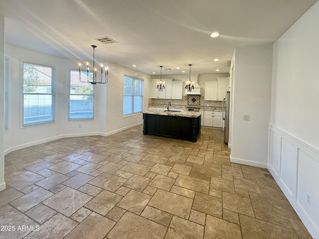 kitchen with an island with sink, pendant lighting, stainless steel fridge, decorative backsplash, and white cabinets