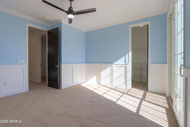 unfurnished bedroom featuring a closet, light colored carpet, crown molding, ceiling fan, and a spacious closet