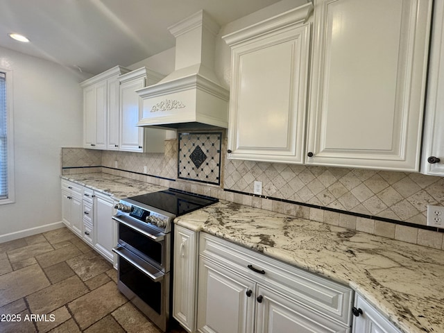 kitchen featuring light stone countertops, range with two ovens, custom exhaust hood, tasteful backsplash, and white cabinetry