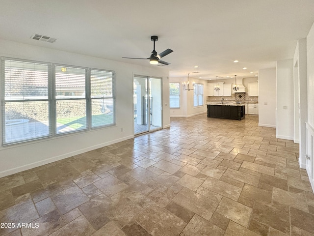 unfurnished living room featuring ceiling fan with notable chandelier and plenty of natural light