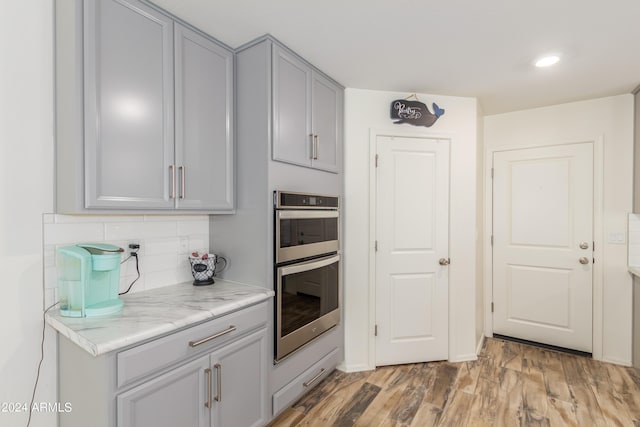 kitchen with light hardwood / wood-style flooring, gray cabinetry, double oven, tasteful backsplash, and light stone counters