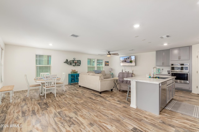 kitchen with sink, light hardwood / wood-style flooring, appliances with stainless steel finishes, gray cabinetry, and an island with sink