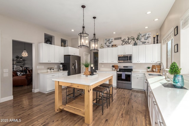 kitchen with a sink, white cabinets, light countertops, appliances with stainless steel finishes, and pendant lighting