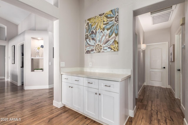 hall featuring dark wood-style floors, visible vents, and baseboards