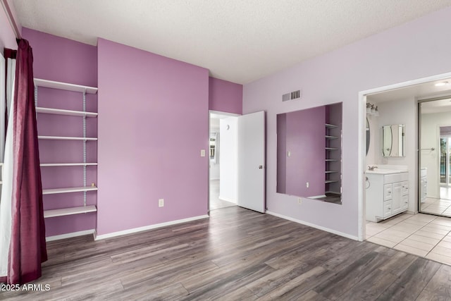 unfurnished bedroom with visible vents, a textured ceiling, wood finished floors, connected bathroom, and baseboards