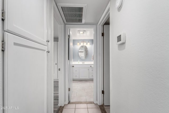 hall featuring light tile patterned floors, a textured wall, visible vents, and a sink