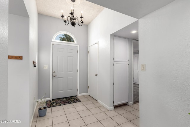 entryway featuring a textured ceiling, light tile patterned flooring, baseboards, and a chandelier