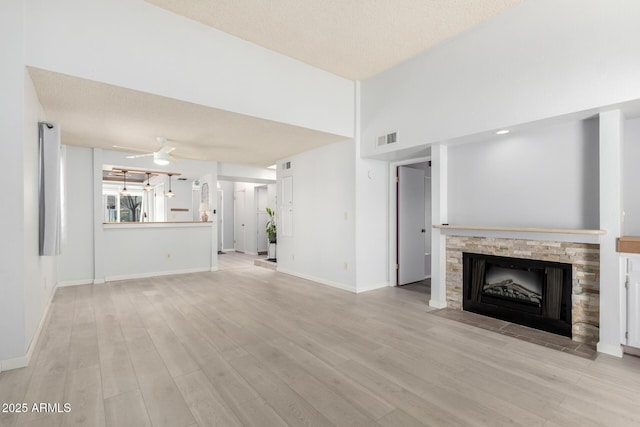 unfurnished living room featuring visible vents, baseboards, ceiling fan, light wood-style flooring, and a fireplace