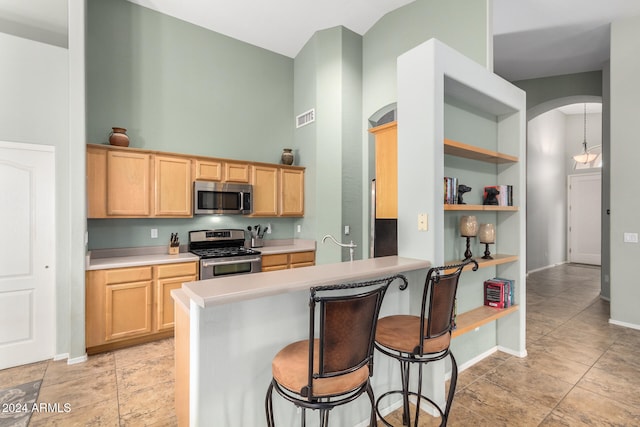 kitchen featuring appliances with stainless steel finishes, light brown cabinetry, hanging light fixtures, a breakfast bar, and kitchen peninsula